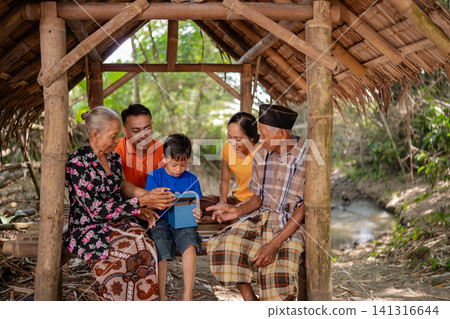 Multigenerational Asian family sharing smiles under bamboo shelter beside river in rural countryside with young boy holding blue box and warm natural light, with family, asian, multigenerational Multigenerational Asian family sharing smiles under bamboo shelter beside river in rural countryside with young boy holding blue box and warm natural light, with family, asian, multigenerational 141316644