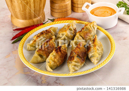 Crispy pan fried dumplings on plate with dipping sauce and chili peppers Crispy pan fried dumplings on plate with dipping sauce and chili peppers 141316986