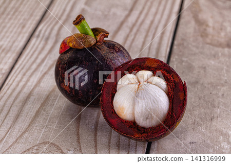 Mangosteen fruit whole and halved on wooden surface Mangosteen fruit whole and halved on wooden surface 141316999