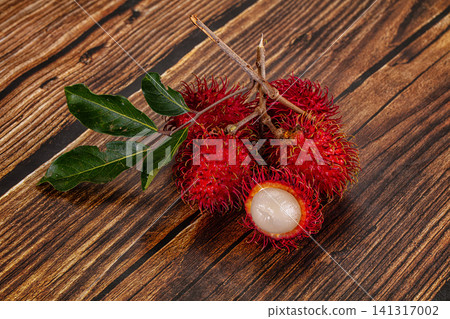 Fresh rambutan fruit cluster with green leaves on rustic wooden surface Fresh rambutan fruit cluster with green leaves on rustic wooden surface 141317002