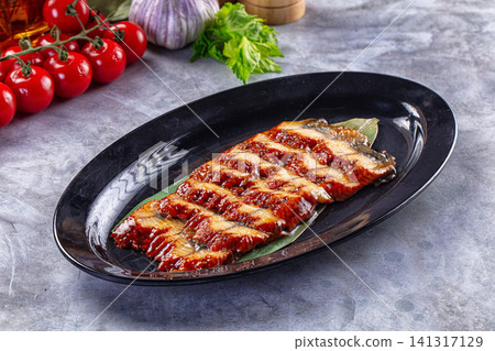Grilled eel on black plate with cherry tomatoes and garlic Grilled eel on black plate with cherry tomatoes and garlic 141317129