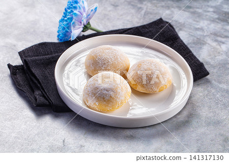 Three powdered mochi desserts on white plate with blue flower 141317130
