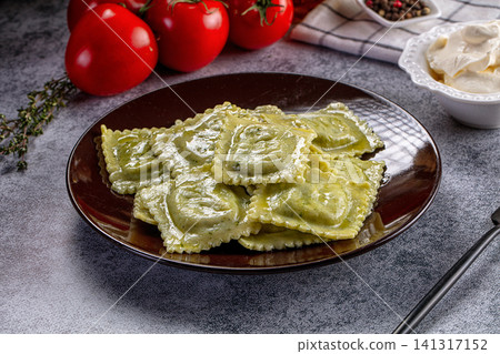 Ravioli with green herb sauce on dark plate with fresh tomatoes and cream 141317152