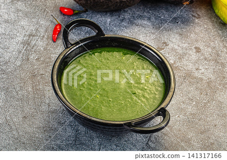 Green spinach cream soup in black ceramic bowl with red chili peppers on rustic surface Green spinach cream soup in black ceramic bowl with red chili peppers on rustic surface 141317166