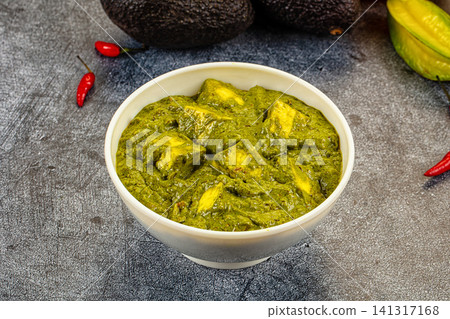 Green spinach curry with paneer in white bowl on dark stone surface with red chili peppers and avocado Green spinach curry with paneer in white bowl on dark stone surface with red chili peppers and avocado 141317168
