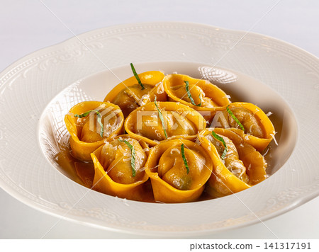 Golden ravioli in white bowl with basil and cheese garnish Golden ravioli in white bowl with basil and cheese garnish 141317191