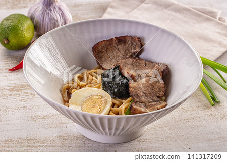 Bowl of ramen with sliced pork, soft boiled egg, nori, and green onions on rustic table with lime and garlic Bowl of ramen with sliced pork, soft boiled egg, nori, and green onions on rustic table with lime and garlic 141317209