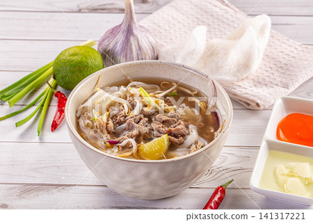 Beef noodle soup with lime garlic and chili on wooden table 141317221