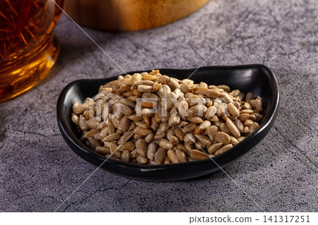 Sunflower seeds in black bowl on textured gray surface with amber glass background Sunflower seeds in black bowl on textured gray surface with amber glass background 141317251