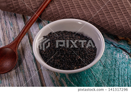 Black sesame seeds in white ceramic bowl with wooden spoon on rustic wooden table Black sesame seeds in white ceramic bowl with wooden spoon on rustic wooden table 141317296