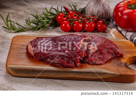 Raw beef cheek on wooden cutting board with rosemary cherry tomatoes garlic and tomato Raw beef cheek on wooden cutting board with rosemary cherry tomatoes garlic and tomato 141317314