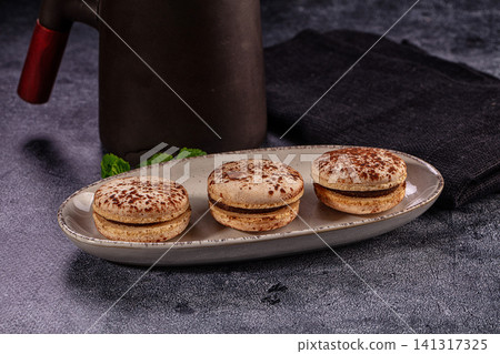 Three chocolate macarons on ceramic plate with dark background and mint garnish Three chocolate macarons on ceramic plate with dark background and mint garnish 141317325