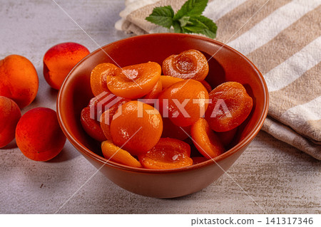 Candied apricot halves in ceramic bowl with fresh apricots and mint on textured surface Candied apricot halves in ceramic bowl with fresh apricots and mint on textured surface 141317346