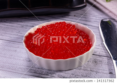 Vibrant red caviar in white ceramic bowl on rustic wooden surface 141317362