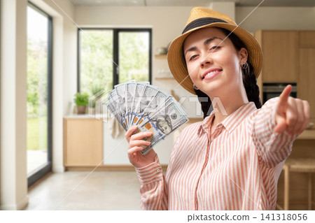 Smiling young Caucasian woman showing dollar bills while standing in a modern new kitchen and looking at the camera. Home financing, mortgage approval, renovation loan, real estate investment Smiling young Caucasian woman showing dollar bills while standing in a modern new kitchen and looking at the camera. Home financing, mortgage approval, renovation loan, real estate investment 141318056