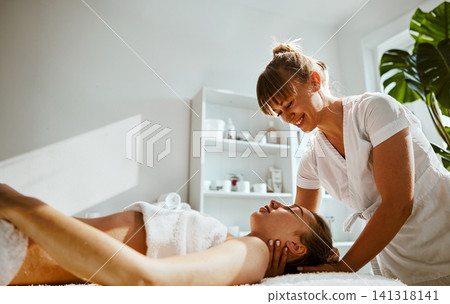 Joyful Spa Connection Smiling Therapist in White Uniform Performs Neck and Shoulder Massage on Relaxed Woman Lying on Table in Bright Biophilic Joyful Spa Connection Smiling Therapist in White Uniform Performs Neck and Shoulder Massage on Relaxed Woman Lying on Table in Bright Biophilic 141318141