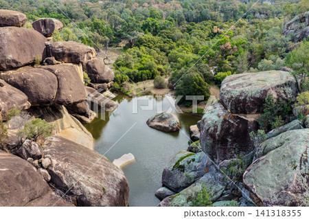 Aerial view of the natural rock pool, elevated viewing platform and striking granite rock formations at Cranky Rock Nature Reserve near Warialda, NSW. Carved by Reedy Creek Aerial view of the natural rock pool, elevated viewing platform and striking granite rock formations at Cranky Rock Nature Reserve near Warialda, NSW. Carved by Reedy Creek 141318355
