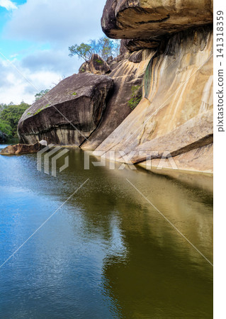 Scenic view of the natural rock pool and impressive granite rock formations at Cranky Rock Nature Reserve near Warialda, NSW. Set beneath a cloudy blue sky and surrounded by native bushland Scenic view of the natural rock pool and impressive granite rock formations at Cranky Rock Nature Reserve near Warialda, NSW. Set beneath a cloudy blue sky and surrounded by native bushland 141318359