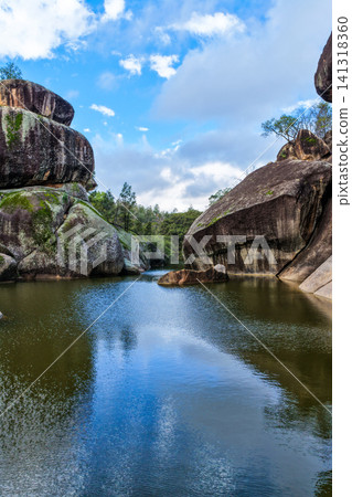 Scenic view of the natural rock pool and impressive granite rock formations at Cranky Rock Nature Reserve near Warialda, NSW. Set beneath a cloudy blue sky and surrounded by native bushland Scenic view of the natural rock pool and impressive granite rock formations at Cranky Rock Nature Reserve near Warialda, NSW. Set beneath a cloudy blue sky and surrounded by native bushland 141318360