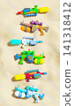 Colorful plastic water guns collection flat lay on sea beach sand, summer vacation background, 3D render 141318412