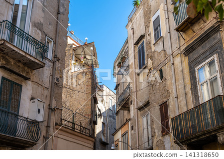 Naples, italy. December 29, 2024. Naples historic center featuring ancient building facades with crumbling plaster, shuttered windows, and traditional balconies under a bright blue sky Naples, italy. December 29, 2024. Naples historic center featuring ancient building facades with crumbling plaster, shuttered windows, and traditional balconies under a bright blue sky 141318650