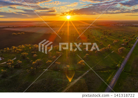 Aerial view capturing sunrise over the farmland surrounding Pilliga, with golden sunrays illuminating the rural landscape to create a peaceful and atmospheric scene in NSW, Australia. Aerial view capturing sunrise over the farmland surrounding Pilliga, with golden sunrays illuminating the rural landscape to create a peaceful and atmospheric scene in NSW, Australia. 141318722