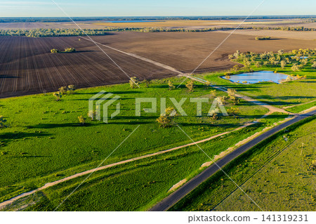Aerial scene showcasing cultivated farmland surrounded by a lush green landscape, highlighting the striking patterns, textures and rich colours of the rural countryside in NSW, Australia. Aerial scene showcasing cultivated farmland surrounded by a lush green landscape, highlighting the striking patterns, textures and rich colours of the rural countryside in NSW, Australia. 141319231