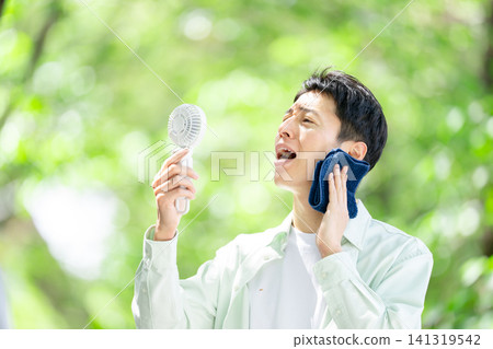 A man holding a portable fan during the intense heat. A man holding a portable fan during the intense heat. 141319542