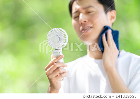 A man holding a portable fan during the intense heat. A man holding a portable fan during the intense heat. 141319553