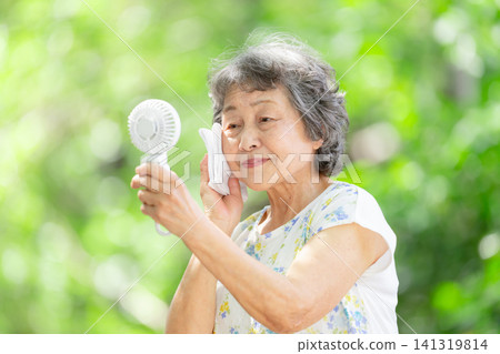 Senior woman, electric fan, fresh green leaves Senior woman, electric fan, fresh green leaves 141319814