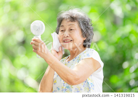 Senior woman, electric fan, fresh green leaves Senior woman, electric fan, fresh green leaves 141319815