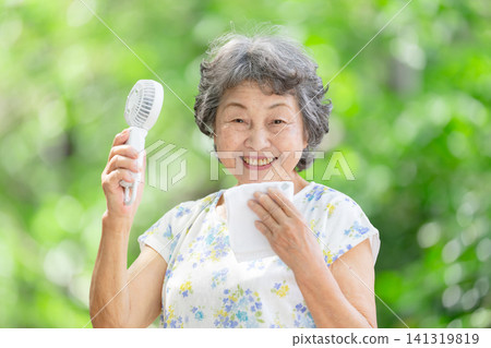 Senior woman, electric fan, fresh green leaves Senior woman, electric fan, fresh green leaves 141319819