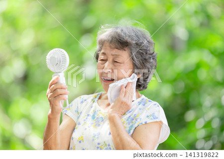 Senior woman, electric fan, fresh green leaves Senior woman, electric fan, fresh green leaves 141319822