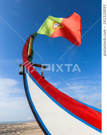A close up of a traditional Arte Xavega boat bow with the Portuguese flag waving against a bright blue sky at a coastal beach in Ovar Portugal A close up of a traditional Arte Xavega boat bow with the Portuguese flag waving against a bright blue sky at a coastal beach in Ovar Portugal 141320093