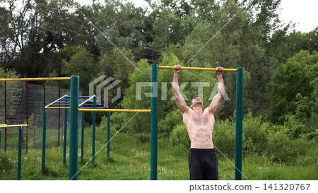 Muscular athlete doing pull ups on horizontal bar at sports ground. Young shirtless sportsman exercising at nature. Strong sporty man training outdoor. Concept of healthy and active lifestyle. Slow mo Muscular athlete doing pull ups on horizontal bar at sports ground. Young shirtless sportsman exercising at nature. Strong sporty man training outdoor. Concept of healthy and active lifestyle. Slow mo 141320767