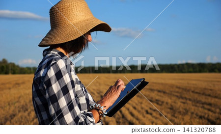 Adult farmer using digital tablet at wheat meadow on sunny day. Female agronomist monitoring harvest at barley field. Beautiful scenic landscape. Concept of agricultural business. Slow motion Adult farmer using digital tablet at wheat meadow on sunny day. Female agronomist monitoring harvest at barley field. Beautiful scenic landscape. Concept of agricultural business. Slow motion 141320788