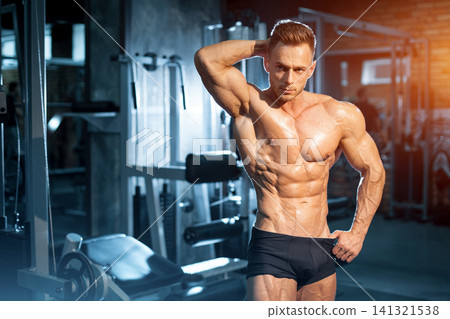 young athletic bodybuilder sportsman posing with torso in gym after workout young athletic bodybuilder sportsman posing with torso in gym after workout 141321538