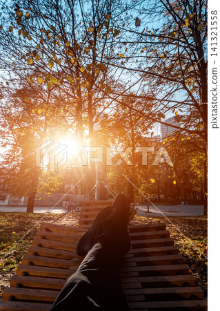 person resting in wooden hammock or bench in autumn park at sunset person resting in wooden hammock or bench in autumn park at sunset 141321558
