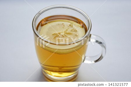 A clear glass mug of hot tea. A round slice of lemon floats in the drink A clear glass mug of hot tea. A round slice of lemon floats in the drink 141321577