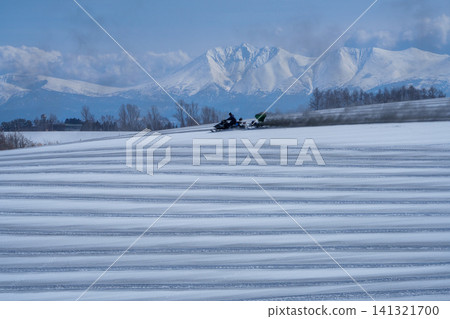 北海道美瑛的農民在白雪皚皚的田野上撒融雪劑；十勝山脈和田野迎接春天。 141321700