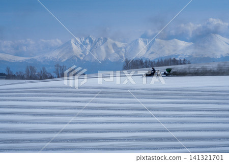 北海道美瑛的農民在白雪皚皚的田野上撒融雪劑；十勝山脈和田野迎接春天。 141321701