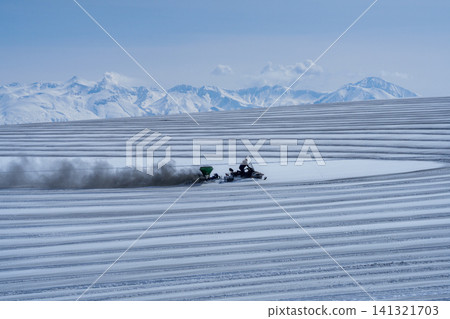 北海道美瑛的農民在白雪皚皚的田野上撒融雪劑；十勝山脈和田野迎接春天。 141321703