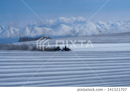北海道美瑛的農民在白雪皚皚的田野上撒融雪劑;十勝山脈和田野迎接春天。 北海道美瑛的農民在白雪皚皚的田野上撒融雪劑;十勝山脈和田野迎接春天。 141321707