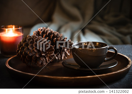 Cup of coffee with pine cone and candle in cozy interior Cup of coffee with pine cone and candle in cozy interior 141322002