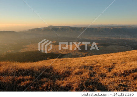從沐浴在夕陽的金色草地上眺望阿蘇市的米塚和火山口景觀。 從沐浴在夕陽的金色草地上眺望阿蘇市的米塚和火山口景觀。 141322180