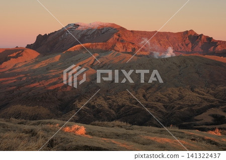 Wintertime Aso Mountains: Peaks Takadake and Nakadake, bathed in the red glow of the setting sun, and plumes of smoke rising from the craters. Wintertime Aso Mountains: Peaks Takadake and Nakadake, bathed in the red glow of the setting sun, and plumes of smoke rising from the craters. 141322437