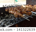Succulent chunks of marinated meat are being grilled on metal skewers over hot grey coals. The traditional shashlik is cooking slowly outdoors, developing a delicious roasted crust on the barbecue 141322639