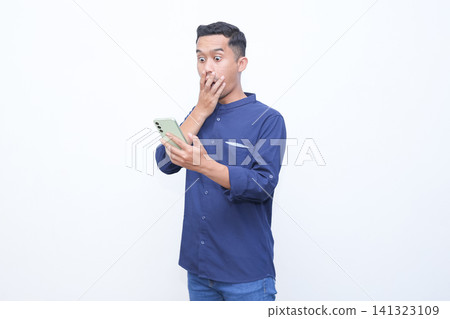 Man holds phone, hand covers mouth in shock. His eyes widen, eyebrows raised. White background isolates the emotion clearly. Ideal for stories of surprise or unexpected news. Man holds phone, hand covers mouth in shock. His eyes widen, eyebrows raised. White background isolates the emotion clearly. Ideal for stories of surprise or unexpected news. 141323109