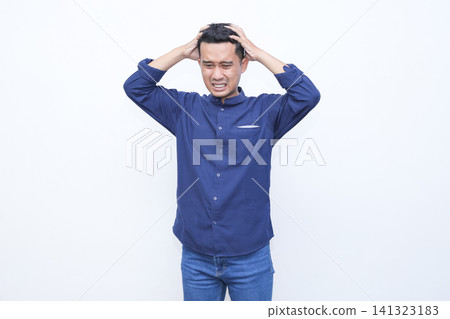 Man grips his head, showing frustration or stress. His face contorts, eyes close, brows furrow. Blue shirt and jeans contrast clean white backdrop. Ideal for stress, deadline Man grips his head, showing frustration or stress. His face contorts, eyes close, brows furrow. Blue shirt and jeans contrast clean white backdrop. Ideal for stress, deadline 141323183