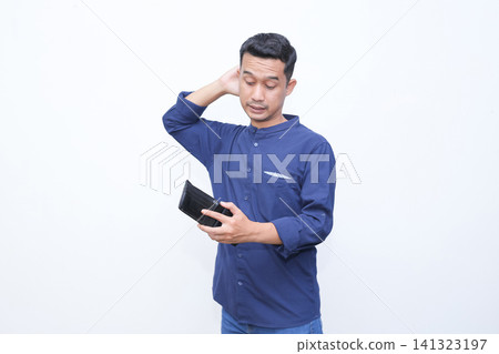 Young man holds wallet, touches forehead in stress. He wears blue shirt, shows frustration or disappointment. Blank background emphasizes emotional moment. Ideal for financial struggles Young man holds wallet, touches forehead in stress. He wears blue shirt, shows frustration or disappointment. Blank background emphasizes emotional moment. Ideal for financial struggles 141323197